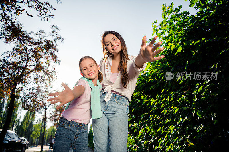 两个开朗可爱的姐妹的肖像，露齿微笑，举起双手欢迎您在市区户外休闲散步