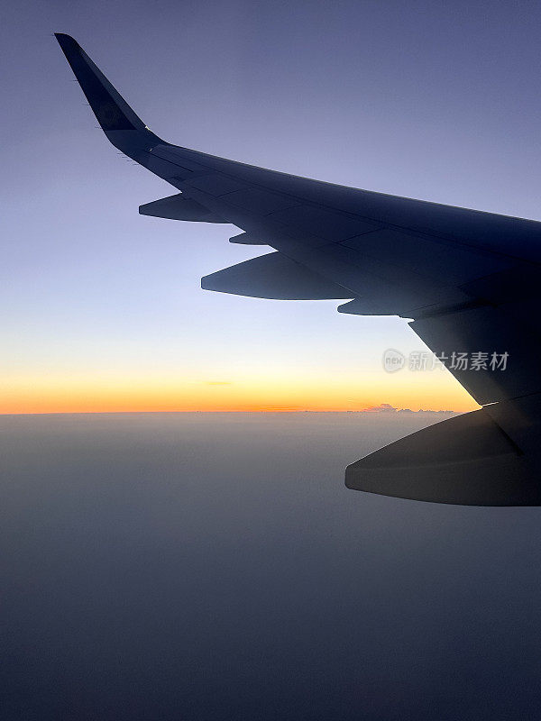 从飞机窗口看的特写图像，在云层上看到的飞机机翼，蓬松的白云，小翼和板条，橙色的日落，重点在前景