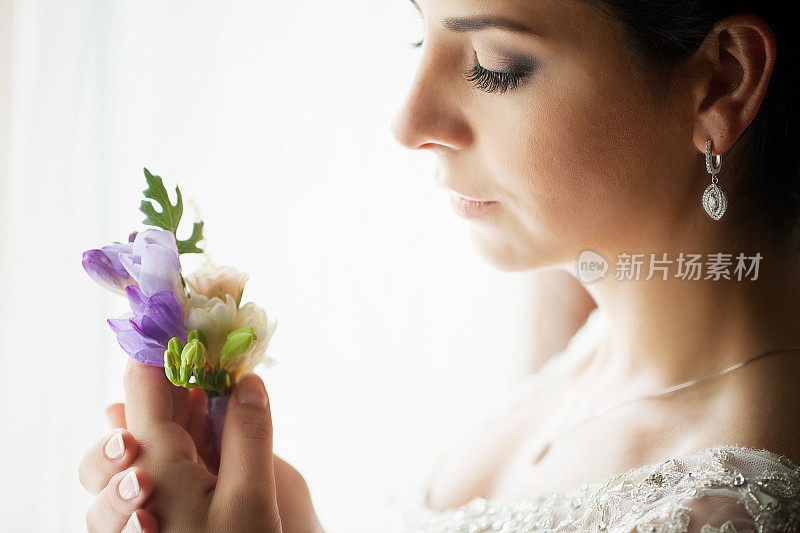 快乐的新娘穿着婚纱，带着鲜花靠近阳光明媚的窗户