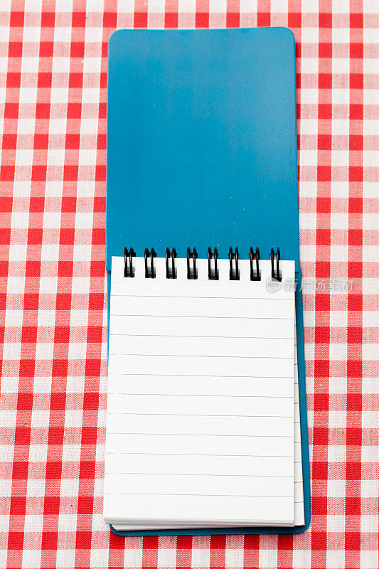 红色格子布桌布上的蓝色螺旋装订笔记本