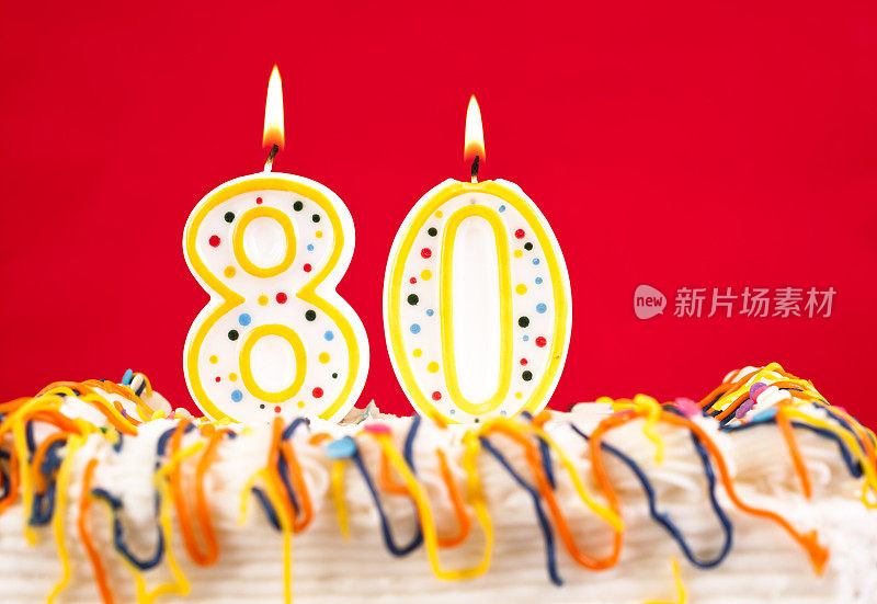 用80号燃烧的蜡烛装饰生日蛋糕。红色的背景。