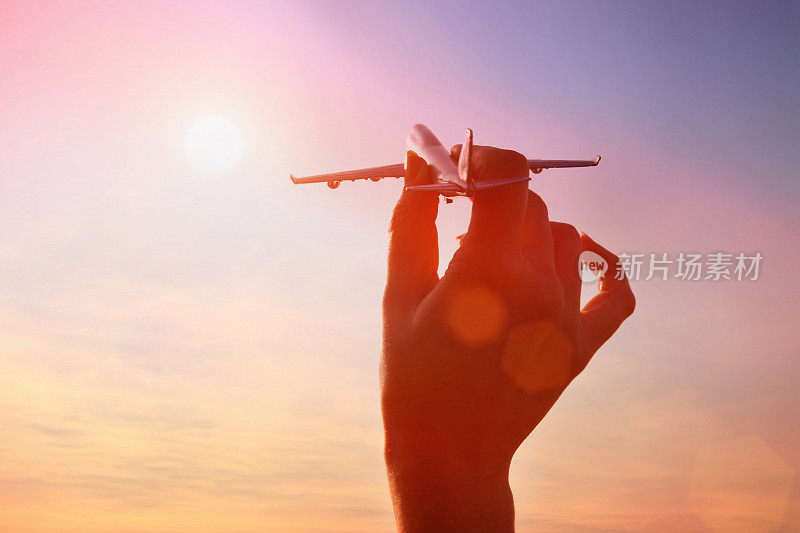 女人牵着飞机模型在夕阳的天空中飞翔