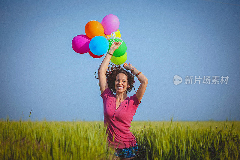 兴高采烈的女人拿着彩色的气球，跑过麦田