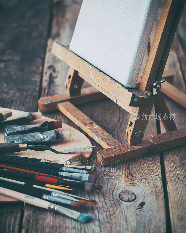 艺术设备:画架上的白色艺术家画布，调色板和艺术家工作室里的画笔。复古的照片。