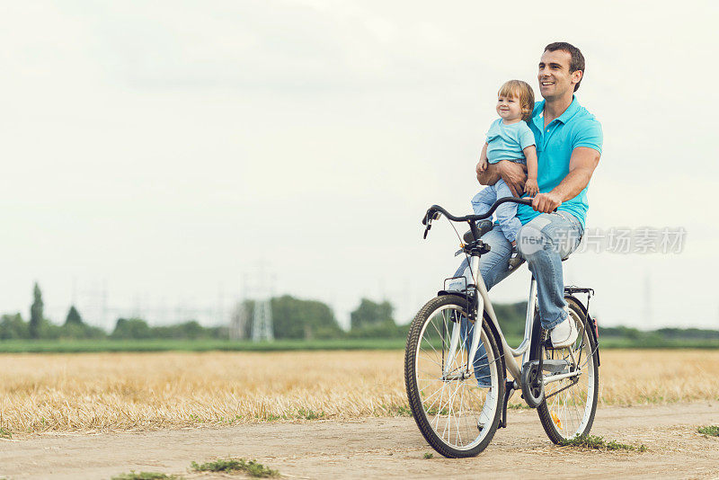 父子俩微笑着骑着自行车在田野里。