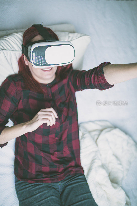 戴着虚拟现实头盔的女人躺在床上。虚拟现实眼镜。