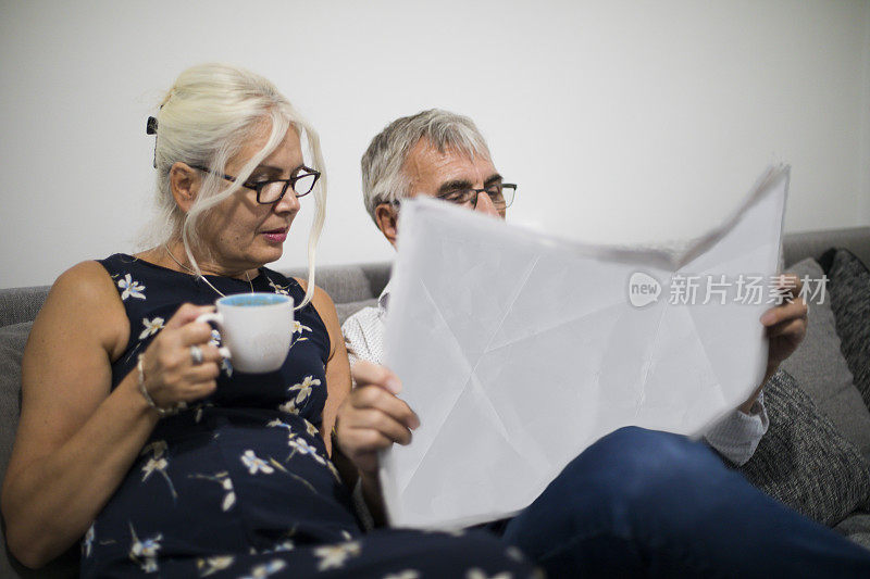 一对老年夫妇在家看报纸，在沙发上休息