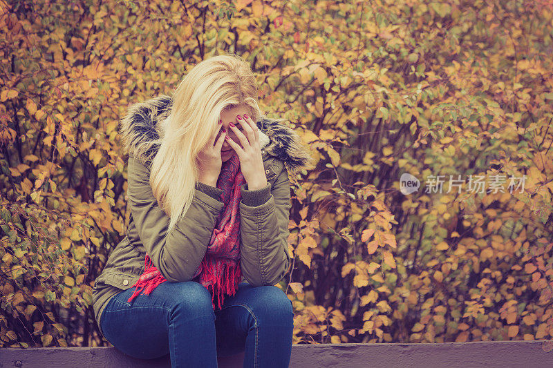 悲伤的女人坐在公园的长椅上藏着脸