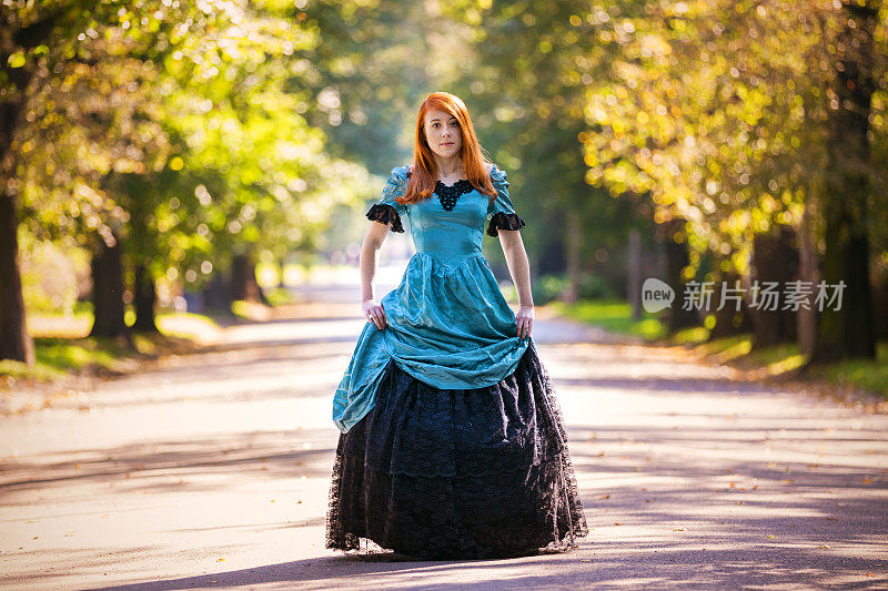 红色头发的女人穿着维多利亚时代的衣服和秋天的公园