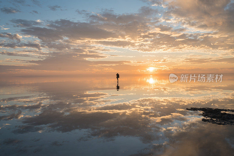 年轻的女摄影师在日落时漫步在盐湖上