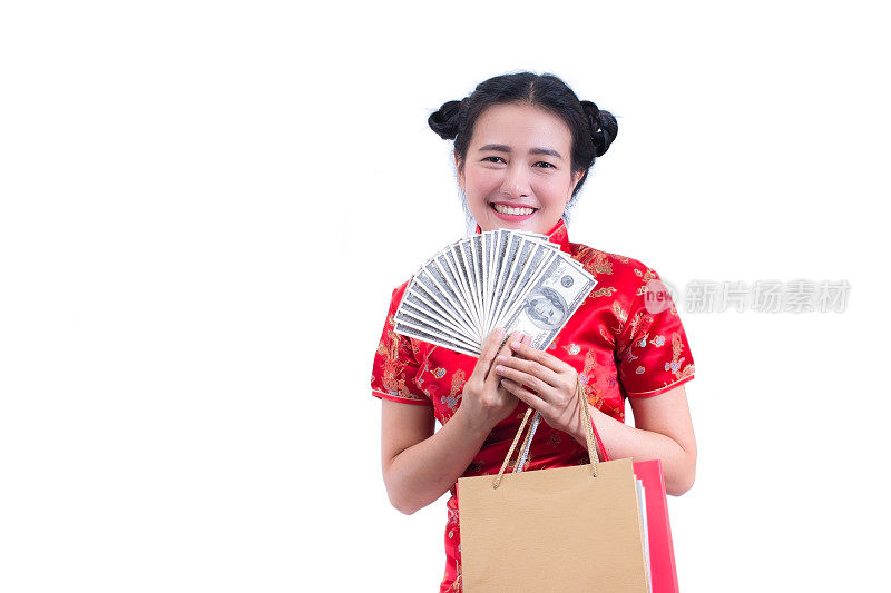 美丽的年轻亚洲妇女穿着中国服装，传统旗袍或旗袍，带着购物袋和美元钞票。春节庆祝活动，新年庆祝活动。