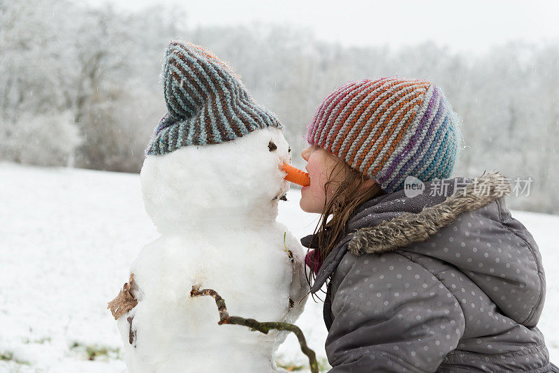 小女孩在玩雪人——它正在吃雪人的胡萝卜鼻子