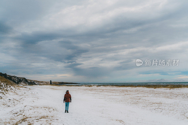 一个女人走在冰岛的黑沙滩上