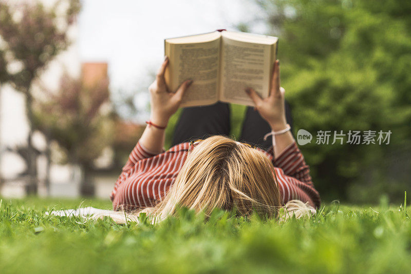 年轻的大一女生躺在公园的草地上看书