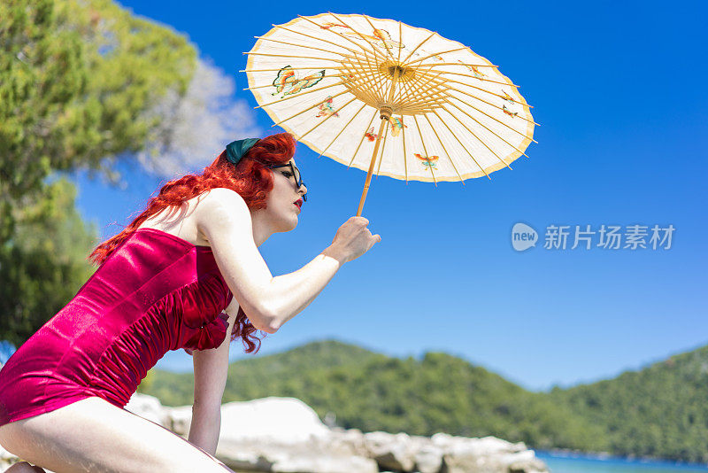侧面的年轻女子与亚洲伞，红色，和一件泳衣的50年代，。Mljet岛上的大湖在克罗地亚的背景中
