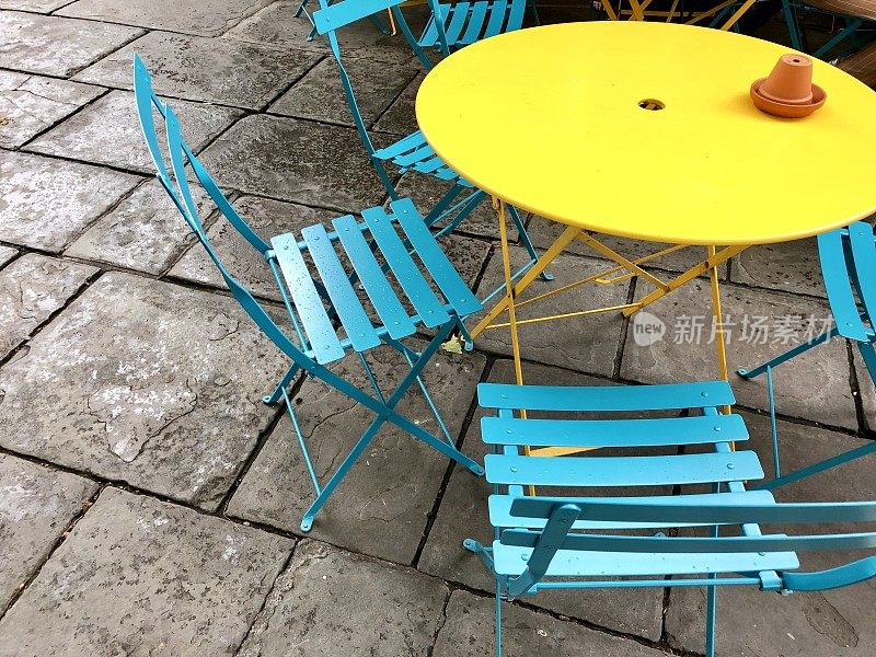 色彩斑斓的图像，圆形的金属和木制的花园庭院桌椅，颜色明亮的彩虹漆，黄色的桌子和绿松石蓝色的椅子