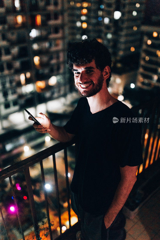 年轻人晚上在住宅阳台上用智能手机