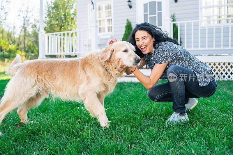 微笑的中年妇女在前院爱抚金毛猎犬