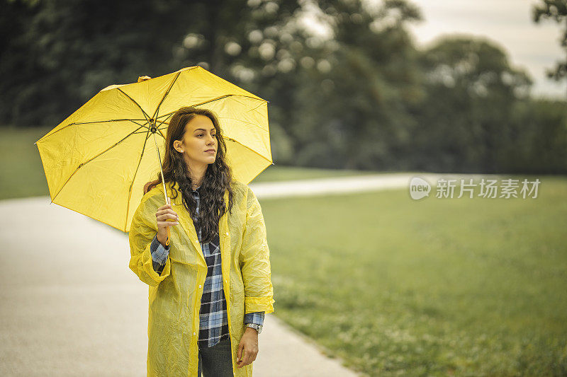 女人穿着雨衣，撑着雨伞，在雨天行走