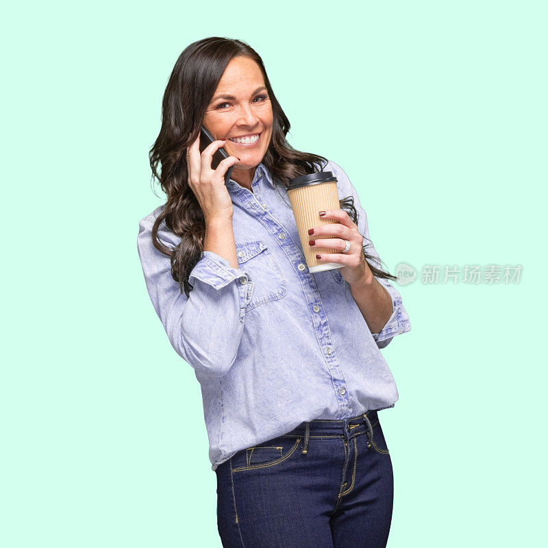 白种女牛仔女穿着纽扣衬衫，拿着咖啡杯和使用手机