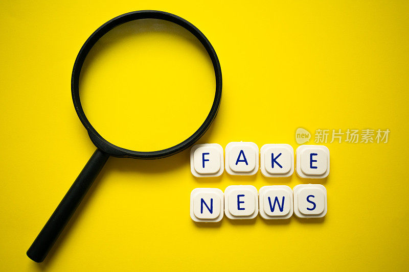 放大镜与“假新闻”信息与字母游戏块，在一个明亮的黄色背景。识别假新闻的重要性概念。