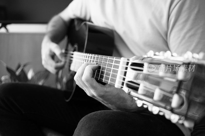 一个在家里弹吉他的人的特写，黑白照片，