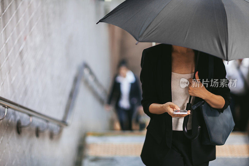 一名女子打着手机撑着雨伞走上地铁楼梯