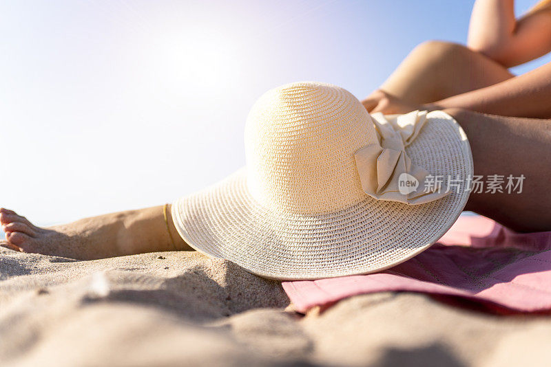 戴草帽的女人坐在海滩上。戴草帽的女人享受着美丽海洋的自由
