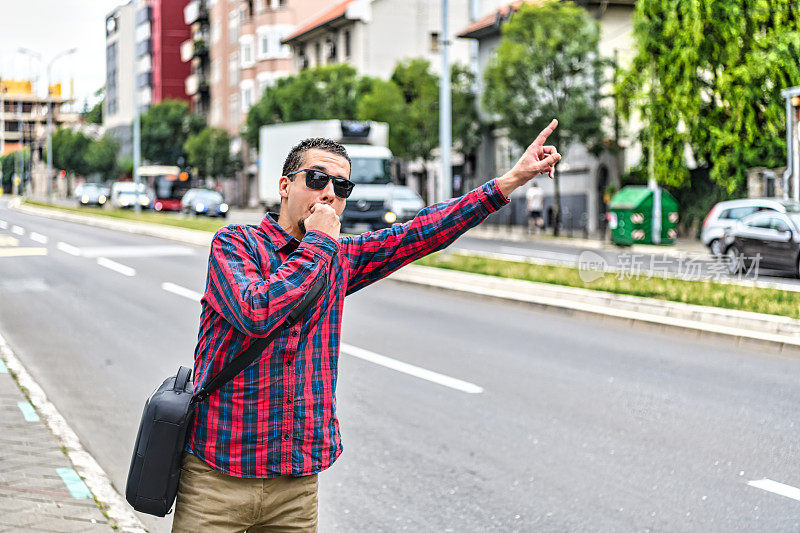 一个戴着太阳镜的商人站在街上挥动手臂想要叫出租车。