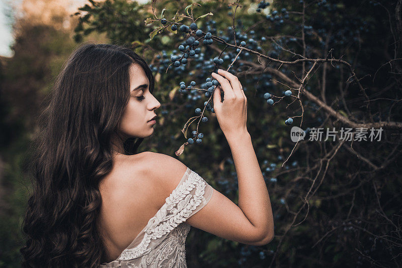 女人长发新娘赤裸的肩膀靠近绿色的灌木蓝莓在夏天