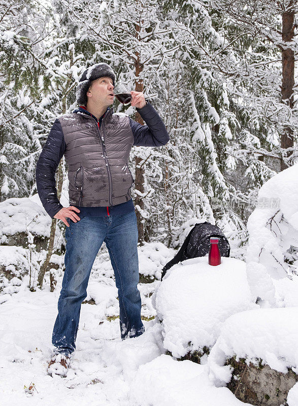 一个男人，一个白种人，穿着冬天的衣服，拿着一杯咖啡，站在一个积雪的森林里。那个人正在休息，享受着宁静。