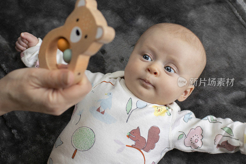 可爱的2个月大的女婴被一个木制玩具迷住了