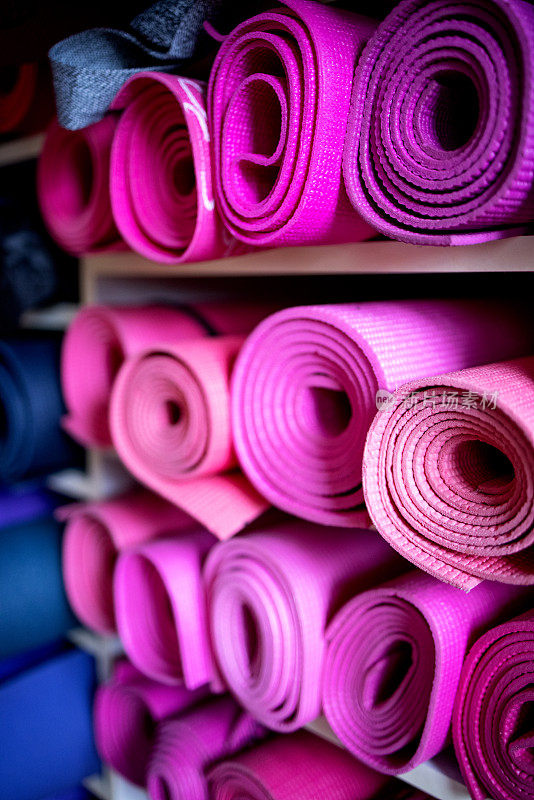 健身房储藏室的架子上有粉色、紫色和蓝色的运动垫