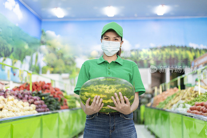 蔬菜水果店的拉丁女店员戴着面具，手里拿着一个大西瓜，眼睛看着镜头