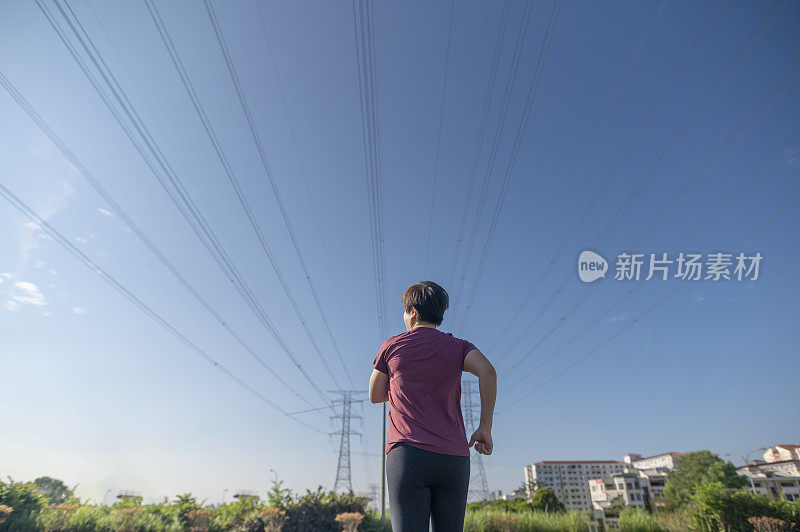 后视图亚洲华人中期成年女性与运动服跑步在早上与电力线蓝天背景