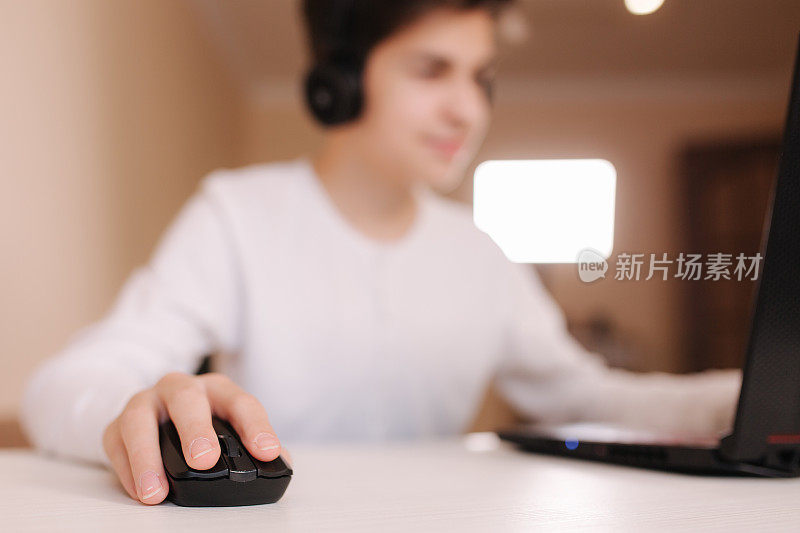 一个十几岁的男孩在白色的房间里玩电脑游戏。玩家在笔记本电脑的网络摄像头上捕捉视频。专注于手