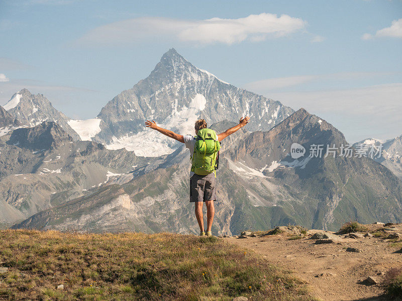 一名男性徒步旅行者站在步道上，双臂向山脉伸展