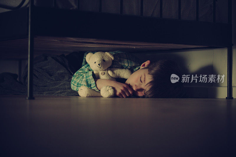 和泰迪熊一起睡在床下的受惊男孩