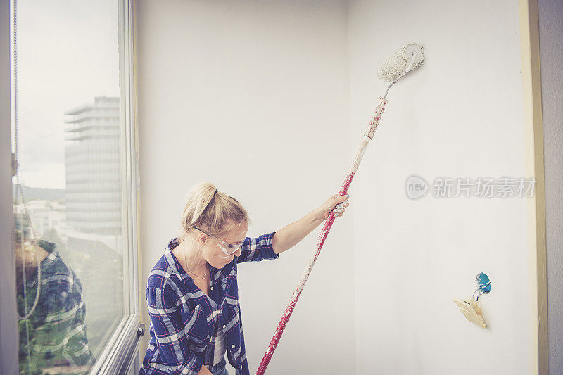 年轻的金发女人正在用油漆滚筒刷墙