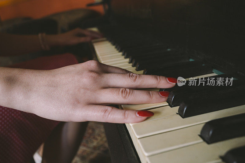 女性的手涂着红色指甲油在钢琴键盘上