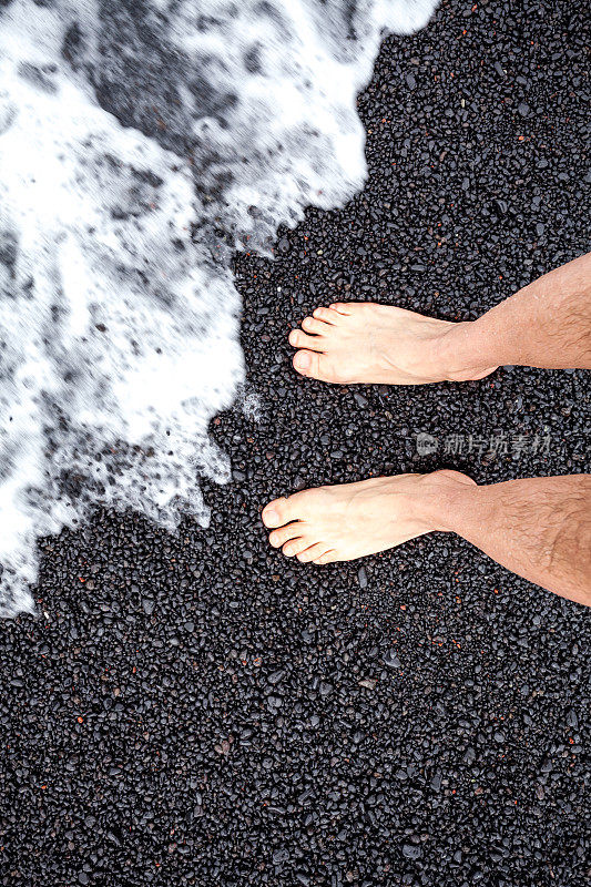 海浪淹没了黑色的海滩与人的脚