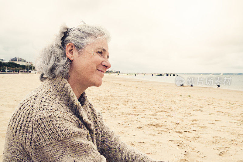 一个满头白发的中年女人坐在海滩上。