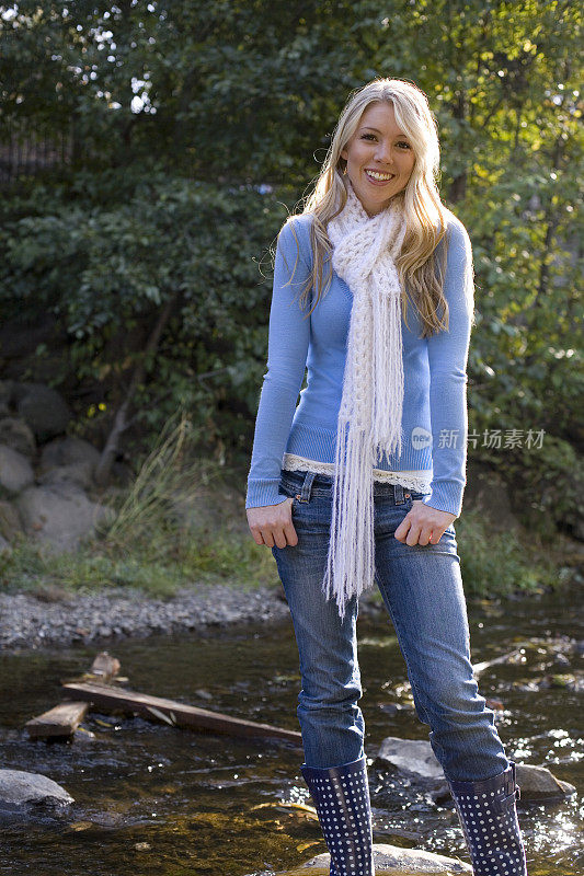 年轻女子在秋天戴着围巾在小溪边