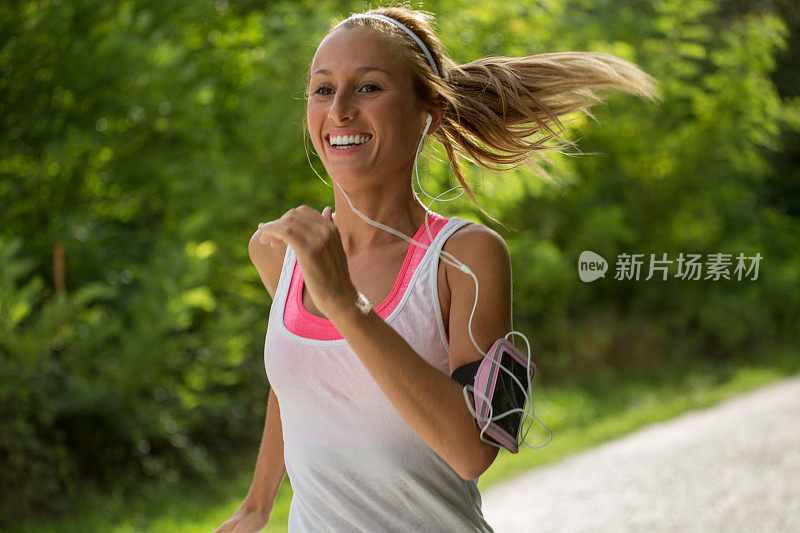 肖像美丽的运动女人听音乐，同时在户外跑步