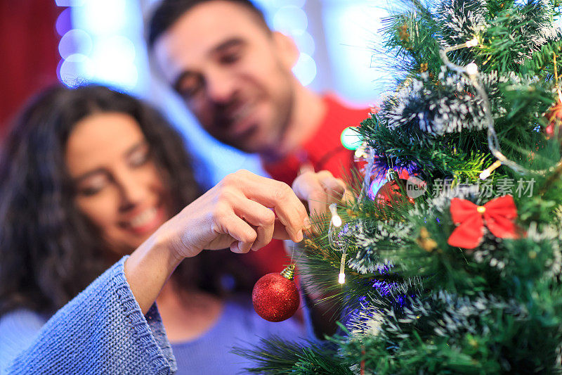 微笑的年轻夫妇在家里装饰圣诞树