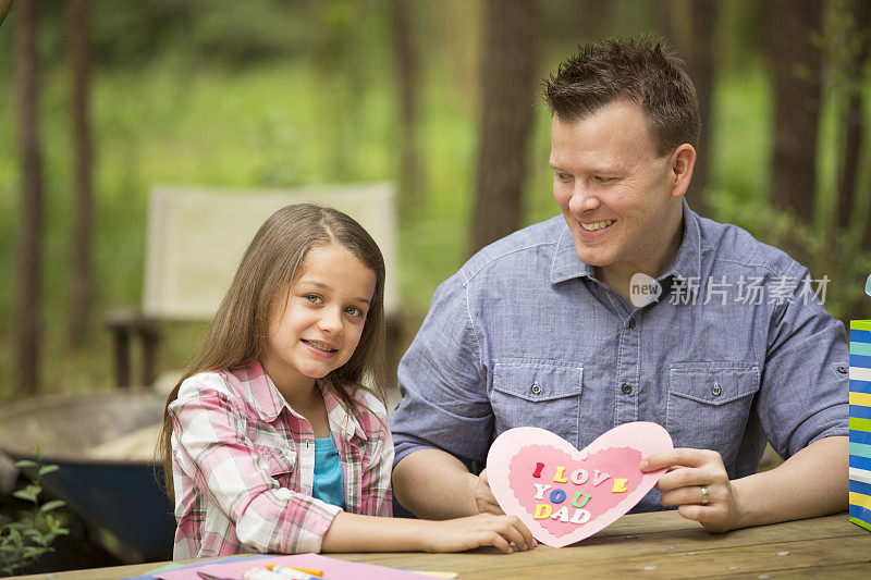 女儿给爸爸看手工制作的父亲节卡片。在户外。孩子,父母。