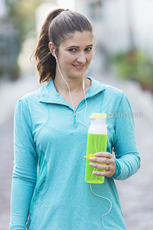 戴着耳机拿着运动饮料的女人