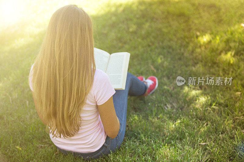 女人坐在绿色的草地上看书