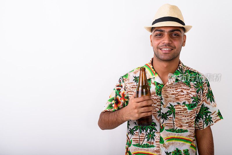 摄影工作室拍摄了一个年轻的印度游客，在白色的背景下，手里拿着一瓶啤酒，面带微笑