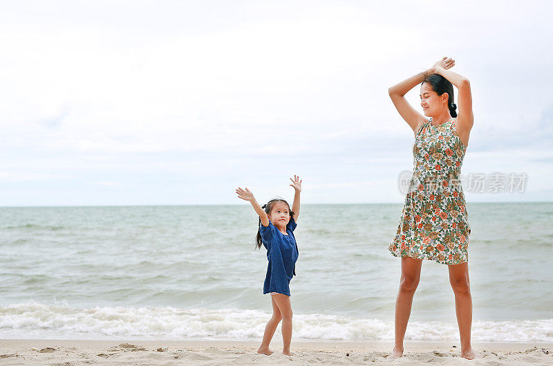 幸福的家庭。妈妈和女儿在海滩上做运动。